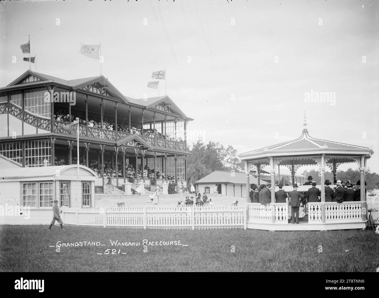 Vista della tribuna e della rotonda della banda presso l'ippodromo di Wanganui, New Zealand Racecourse, veduta della tribuna e della rotonda della banda presso l'ippodromo di Wanganui, New Zealand Racecourse in un giorno di gara. Le bandiere volano sulla tribuna piena di persone, e c'è un gruppo di suonatori che si esibiscono nella band Rotunda Foto Stock