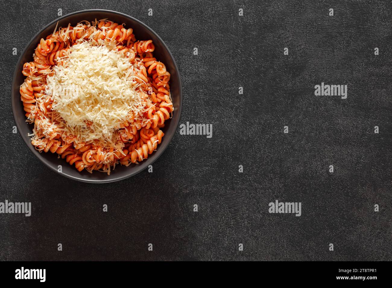 Fusilli, cotti con salsa di pomodoro e parmigiano grattugiato, su sfondo scuro, vista dall'alto, spazio per copiare il testo. Foto Stock