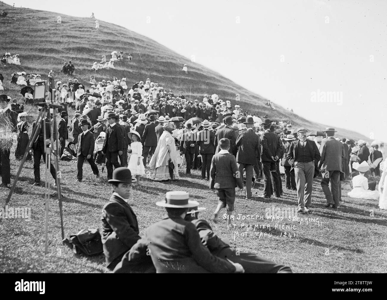 Sir Joseph Ward parla sull'isola di Motutapu, fotografia scattata nel 1910 da William Price. Mostra una folla su una collina sull'isola di Motutapu ascoltando Sir Joseph Ward (fuori vista) parlare a un picnic sull'isola. La fotocamera e il cavalletto possono essere visti a sinistra Foto Stock