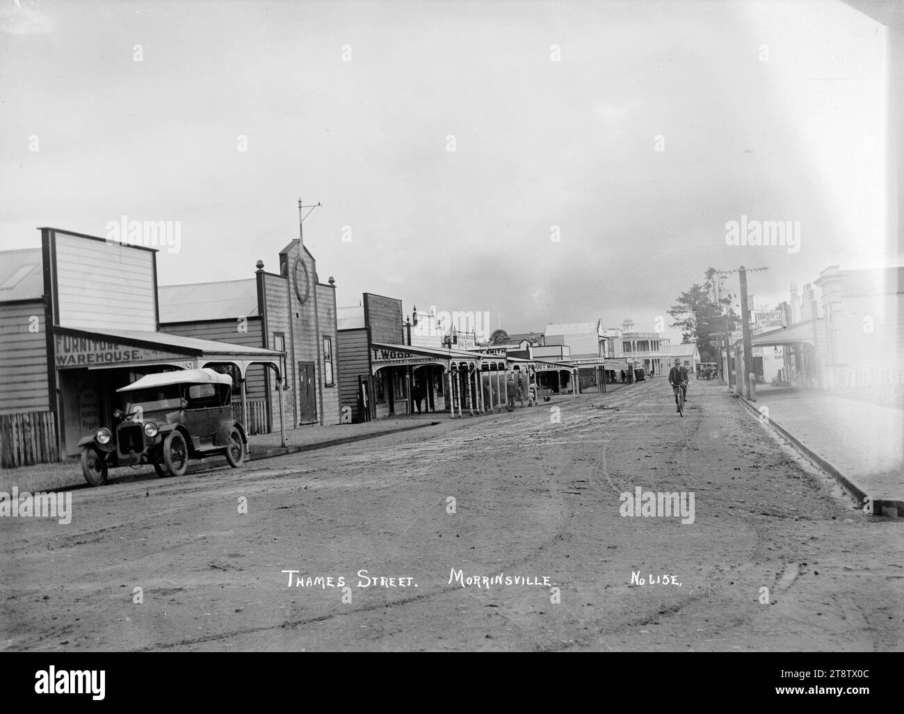 Thames Street, Morrinsville, CA 1916, Thames Street, Morrinsville, mostra una fila di negozi sul lato sinistro della strada e un'auto da turismo parcheggiata (in primo piano a sinistra). Datato dal fatto che i locali commerciali di Thomas Wood (tabacchino e parrucchiere), sono visibili in strada, ed è elencato nel Direttorio dell'ufficio postale di Wise nel 1916 (non nel 1910, 1913 o 1918) Foto Stock