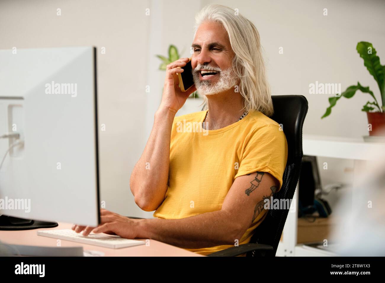 Programmatore di computer maschio che parla sullo smartphone mentre si utilizza il computer Foto Stock