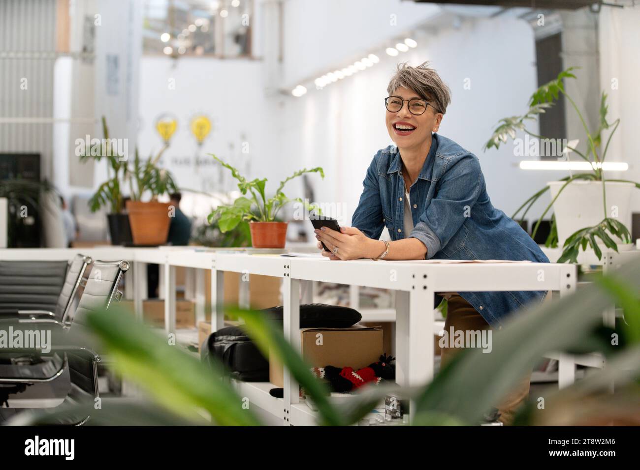 Imprenditrice donna che scorre sullo smartphone mentre si appoggia al tavolo Foto Stock