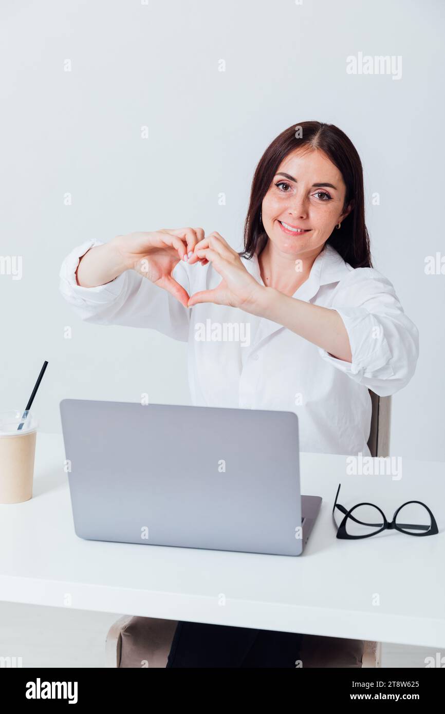 Donna d'affari che mostra il cuore delle mani in ufficio Foto Stock