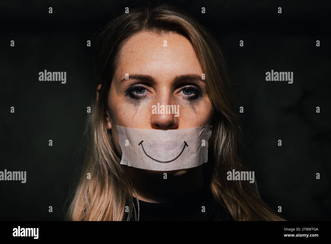 abusi e violenza domestica. triste donna depressa nasconde la bocca dietro un sorriso finto disegnato su nastro di carta. depressione e salute mentale Foto Stock