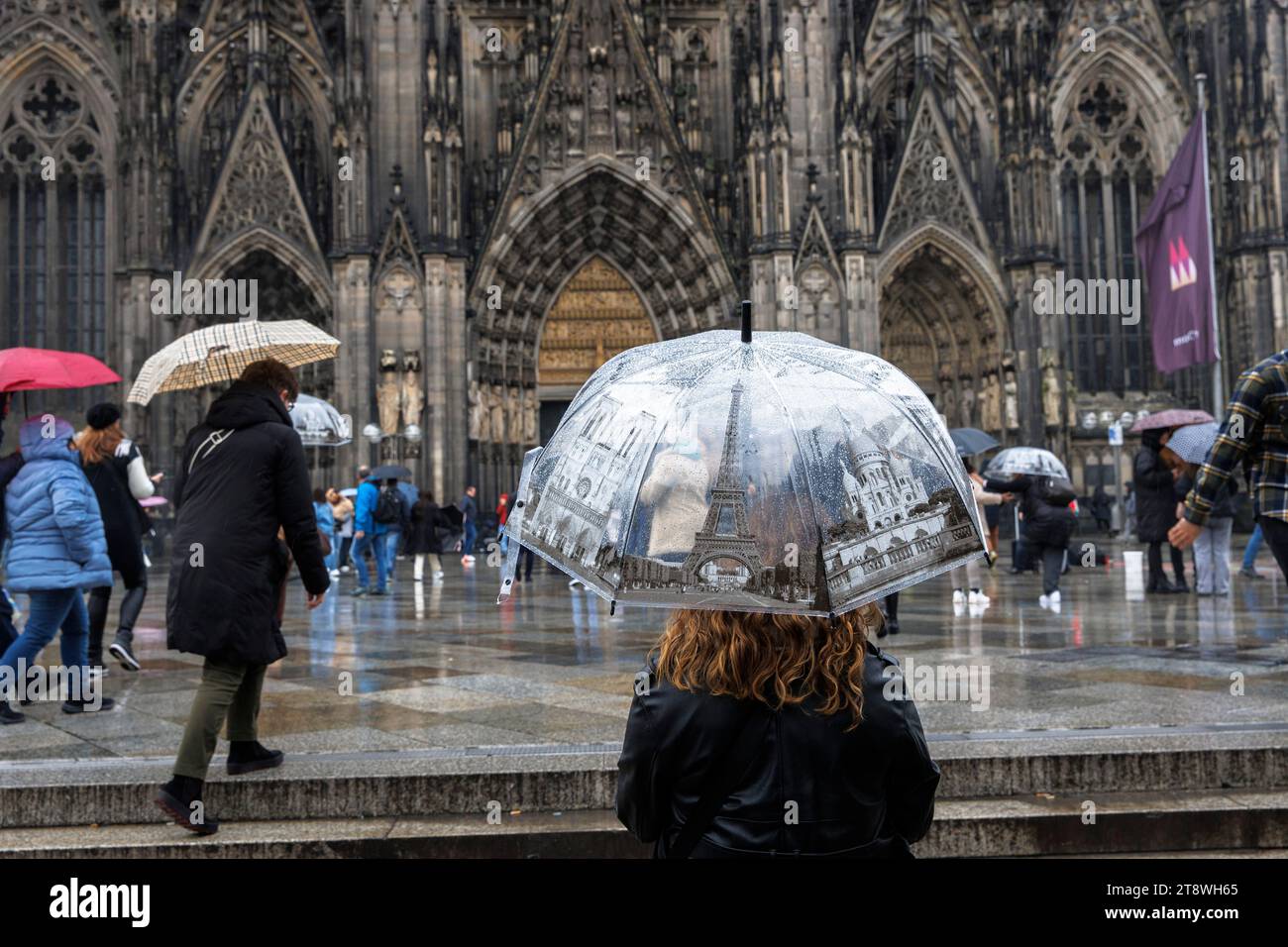 Turista con ombrelloni a tema Parigi di fronte alla cattedrale, Colonia, Germania. Tourist mit Regenschirmen mit Paris Motiven stehen bei Regen vor dem Foto Stock