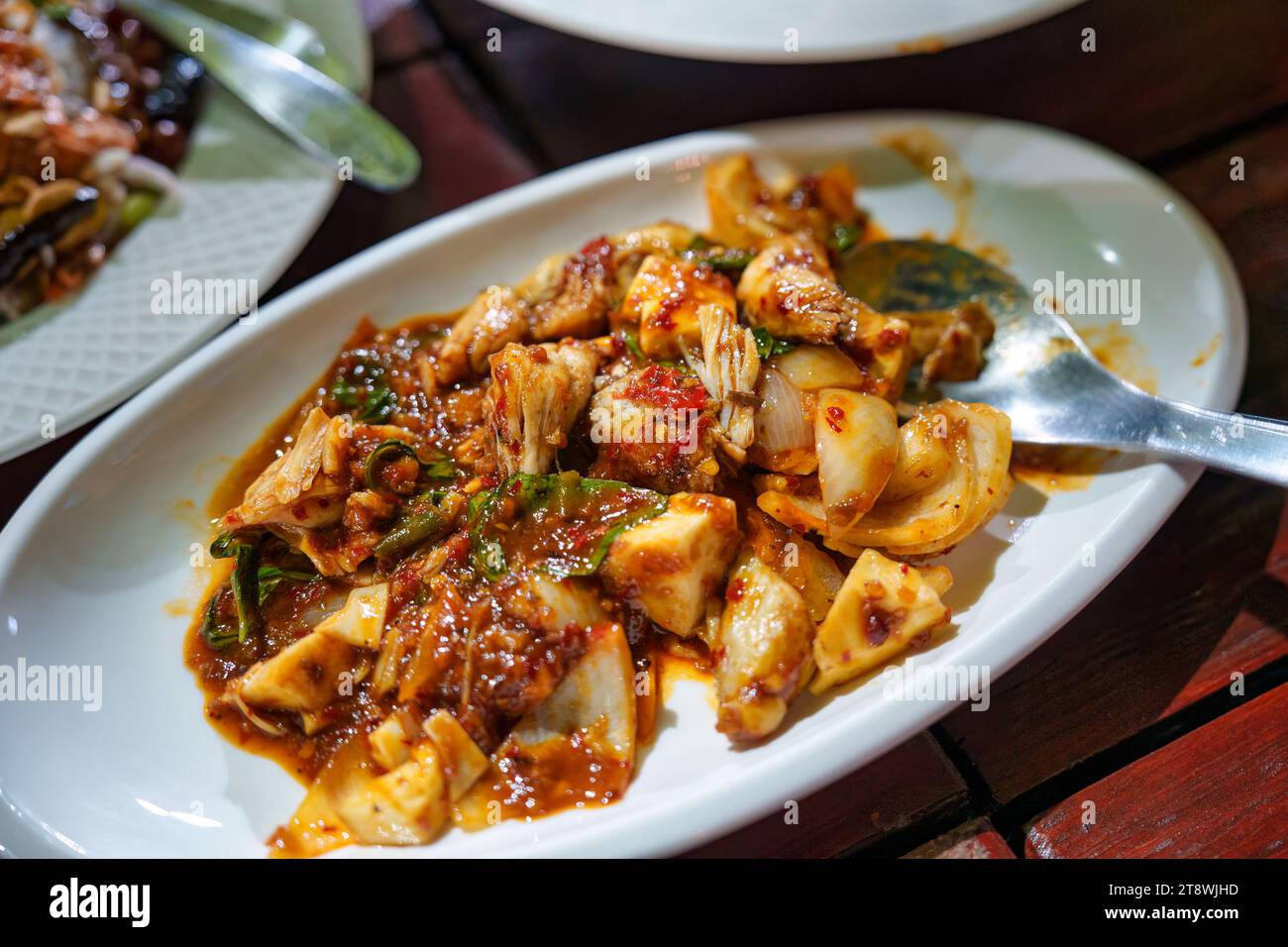 Mescolare la carne di pollo fritta con la salsa al peperoncino e le erbe nel piatto bianco del ristorante tailandese locale Foto Stock