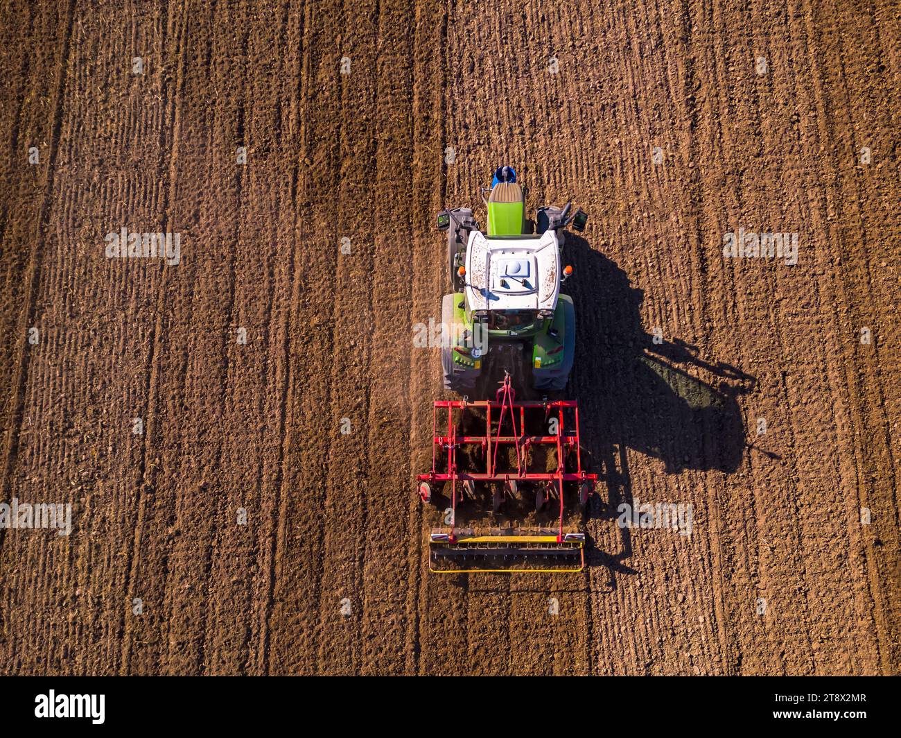 Vista aerea di un trattore verde che ara un campo lasciando i cingoli sul campo Foto Stock