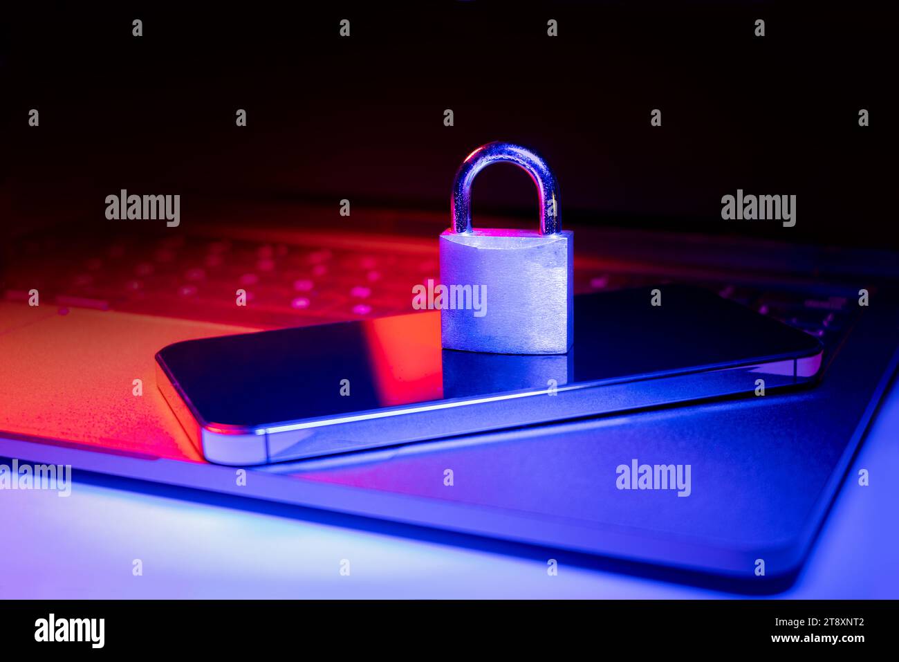 Primo piano di un lucchetto su un computer portatile e un telefono illuminato da luce blu e rossa.phishing, pericolo di cybersicurezza o attacco ransomware. Privacy crittografata Foto Stock