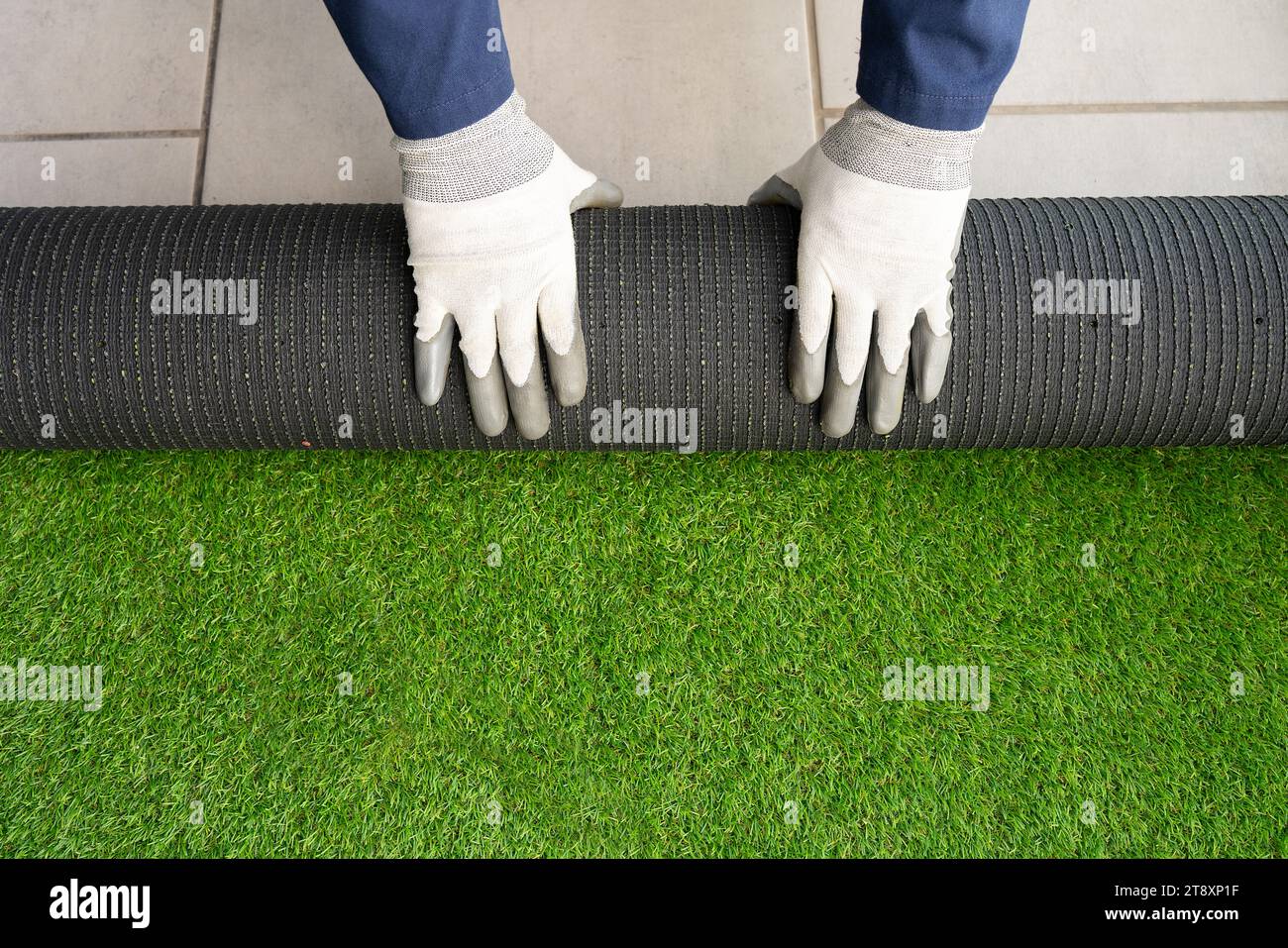 Mani degli uomini che tengono un rotolo di erba artificiale e la installano su una casa. Sfondo erba artificiale. Foto Stock
