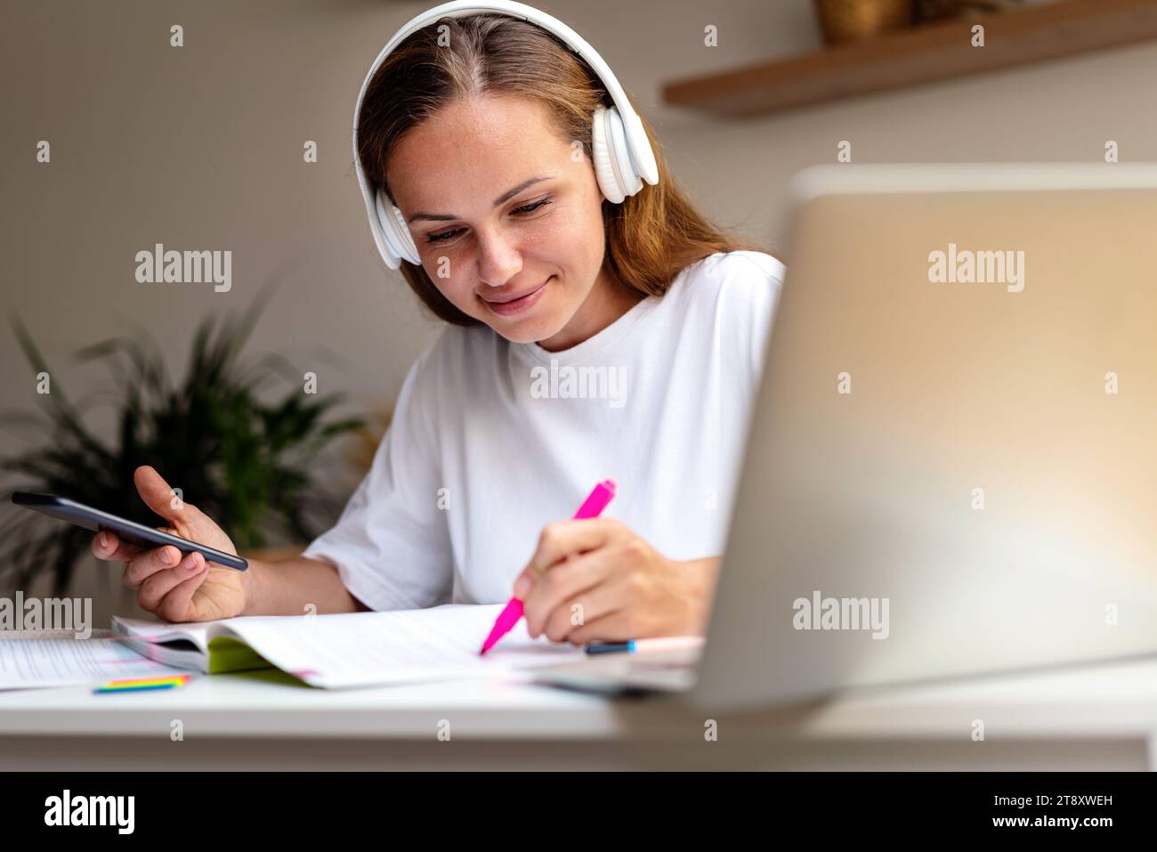 Giovane studentessa che fa i compiti di carta a casa utilizzando cartelle di lavoro e dispositivi digitali. Foto Stock