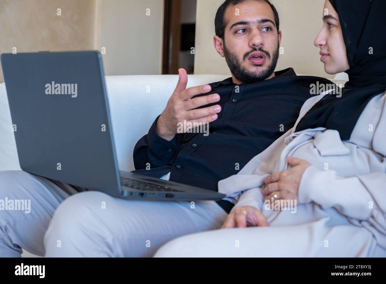 uomini e donne incinte che parlano della gravidanza e di come crescere il bambino mentre usa il notebook in casa indossando il nero e il grigio Foto Stock