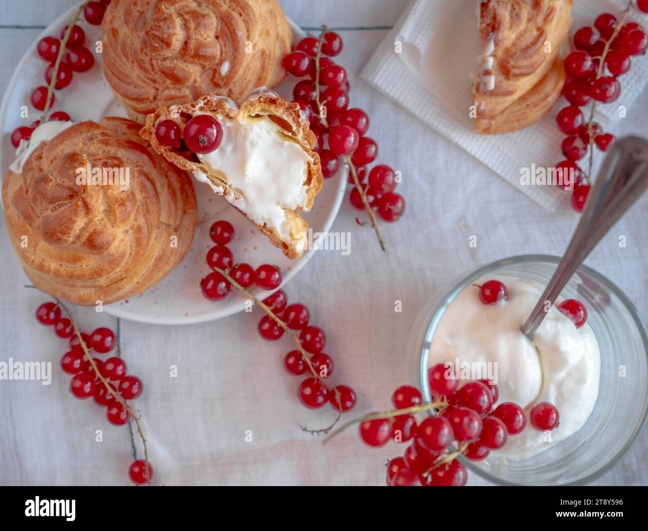 Dolce e delizioso tavolo da dessert con dolce choux rotondo (eclairs) riempito con crema crema pasticcera bianca e decorato con ciuffi di ribes rosso Foto Stock