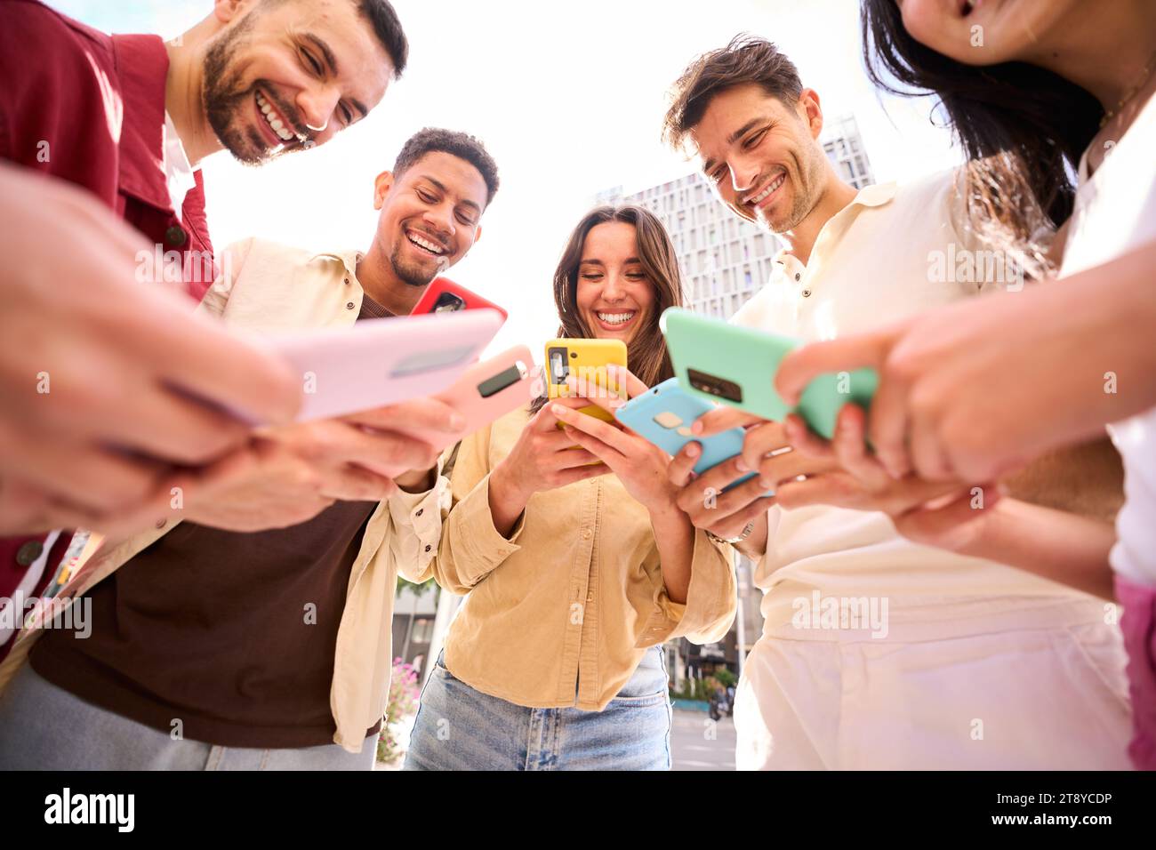 Raggruppa i giovani in cerchio usando i telefoni insieme all'aperto. Amici allegri che si incontrano divertendosi. Foto Stock