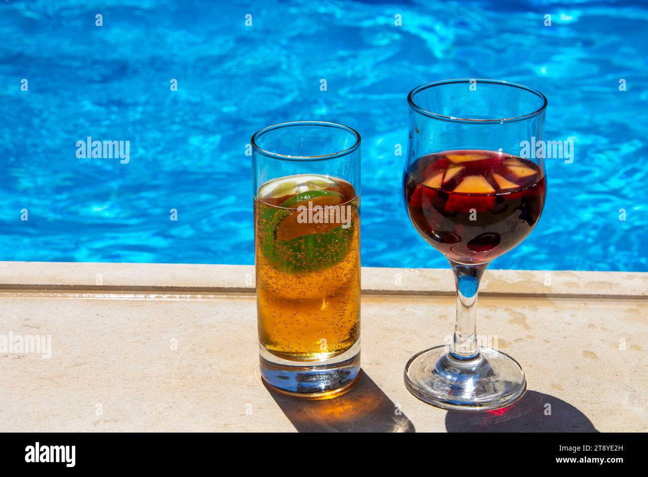 Due bevande rinfrescanti a bordo piscina, un bicchiere di birra e un bicchiere di sangria, sotto il sole luminoso Foto Stock