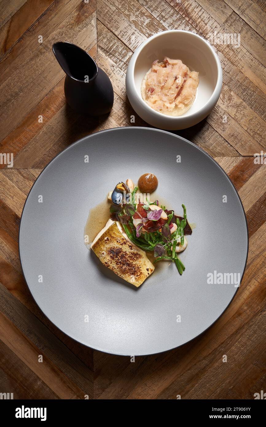 Piatto gourmet di pesce e verdure su piatto di ceramica e tavolo in legno Foto Stock