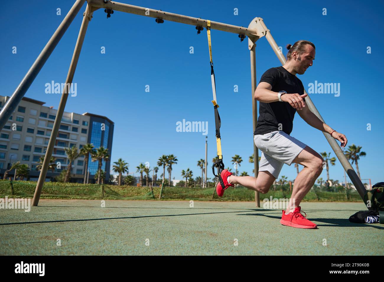 Uomo muscoloso durante l'allenamento fisico allenare il peso corporeo con cinghie di sospensione TRX. Atletico che fa affondi, pompando i muscoli delle gambe. Gente, acti Foto Stock