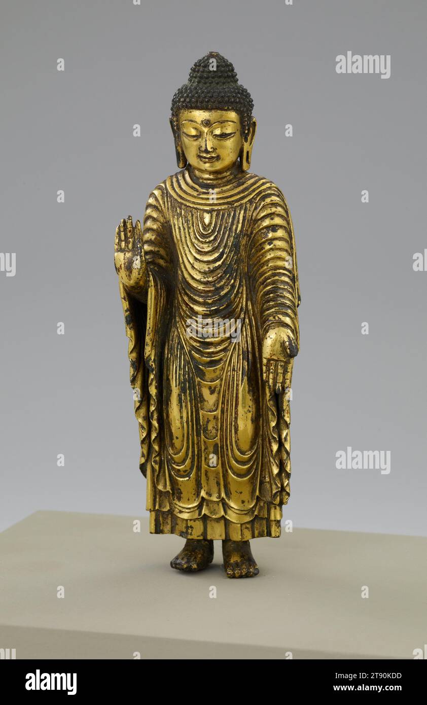Udhyana Buddha, XIV secolo, 5 pollici (12,7 cm), Gilt Bronze, Cina, XIV secolo, questa piccola statua in bronzo dimostra come le immagini e gli stili si diffondono in tutto il mondo buddista. Si dice che la rappresentazione sia basata su una scultura in legno di sandalo commissionata dal re Udhyana in India durante la vita dello storico Buddha (400 a.C. circa). Una copia fu portata in Cina nel 405 e poi trasferita al tempio da Shang Shou an si a Pechino nel 1289. La fusione di questo bronzo in miniatura mostra l'influenza nepalese, un risultato dell'imperatore della dinastia Yuan, Kublai Khan (r. 1260–94) Foto Stock