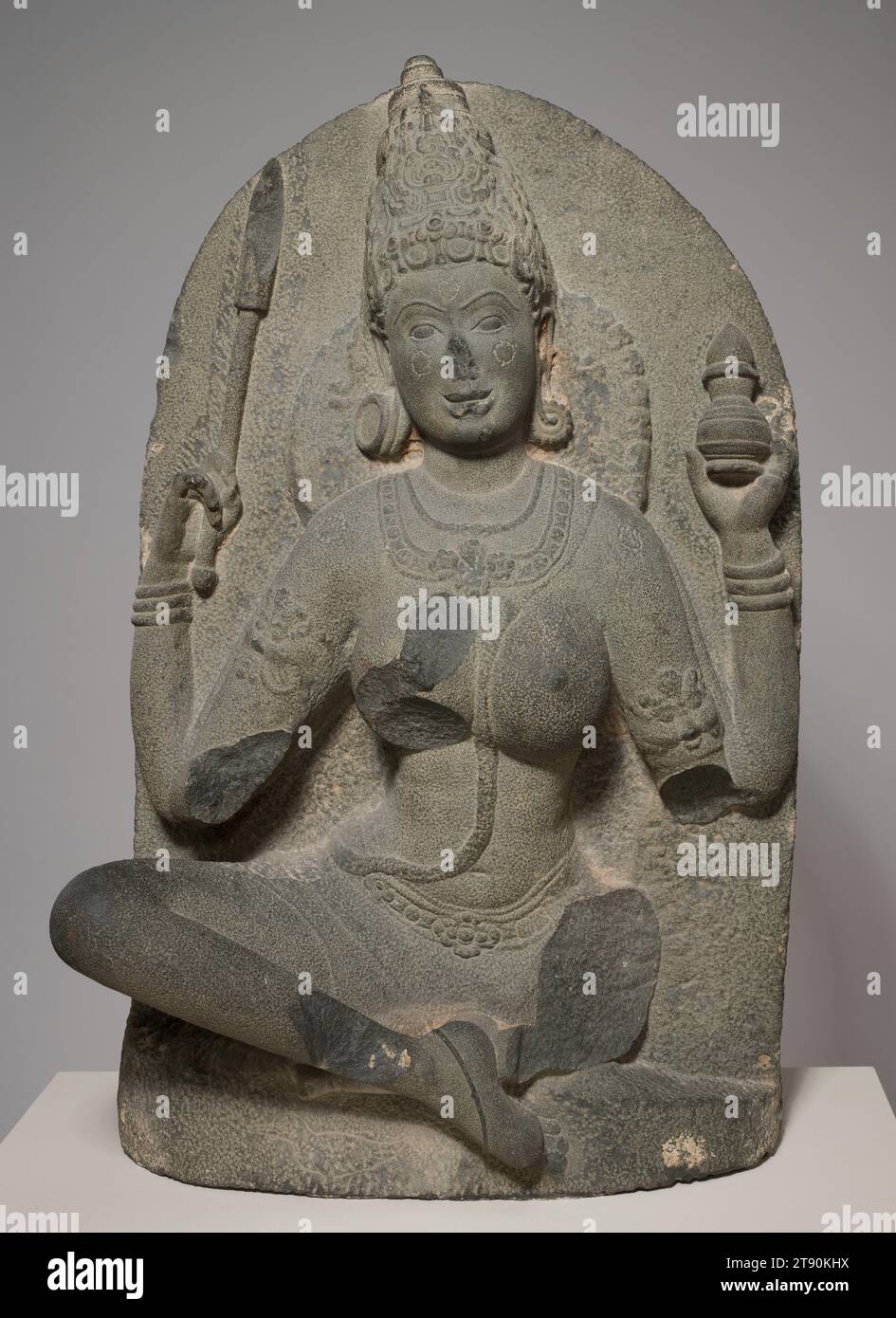 Yogini con barattolo, inizio X secolo, 45 x 28 1/2 x 1/2 pollici (114,3 x 72,39 x 39,37 cm), roccia Ignea, India, periodo Chola, X secolo, in tutto il subcontinente e all'interno delle sue numerose fedi indigene, la dea, o devi, è venerata come una manifestazione di energia femminile che dà la vita. Qui, una dea conosciuta come yogini dimostra con grazia il pieno controllo del respiro e del corpo. Le sue mani tengono un vaso, forse contenente medicine, e una bacchetta, suggerendo le sue capacità curative. Il suo arto inferiore sinistro, ora rotto, avrebbe tenuto una tazza per il cranio per bere liquore o sangue, segnalando la sua ferocia Foto Stock