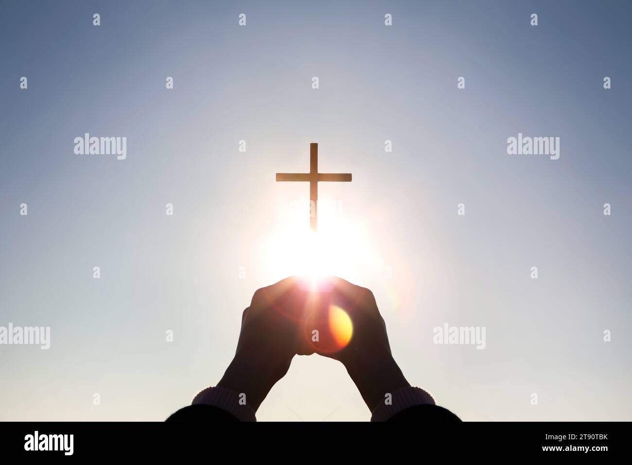 Luce solare brillante e silhouette di mani cristiane che reggono in alto la croce di Gesù Cristo che simboleggia la morte e la resurrezione Foto Stock