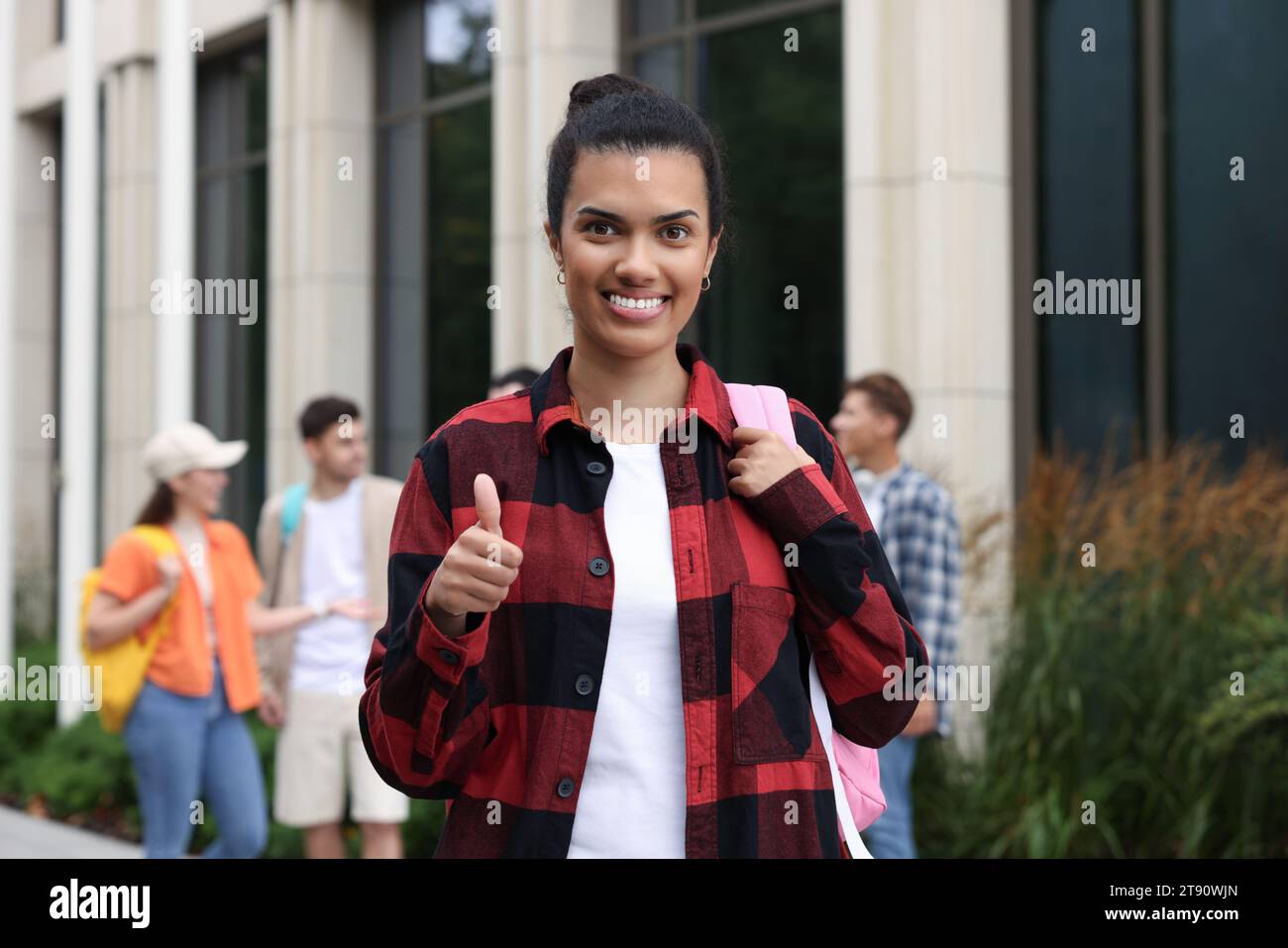 Studente felice con lo zaino che mostra i pollici in alto all'aperto, concentrazione selettiva Foto Stock