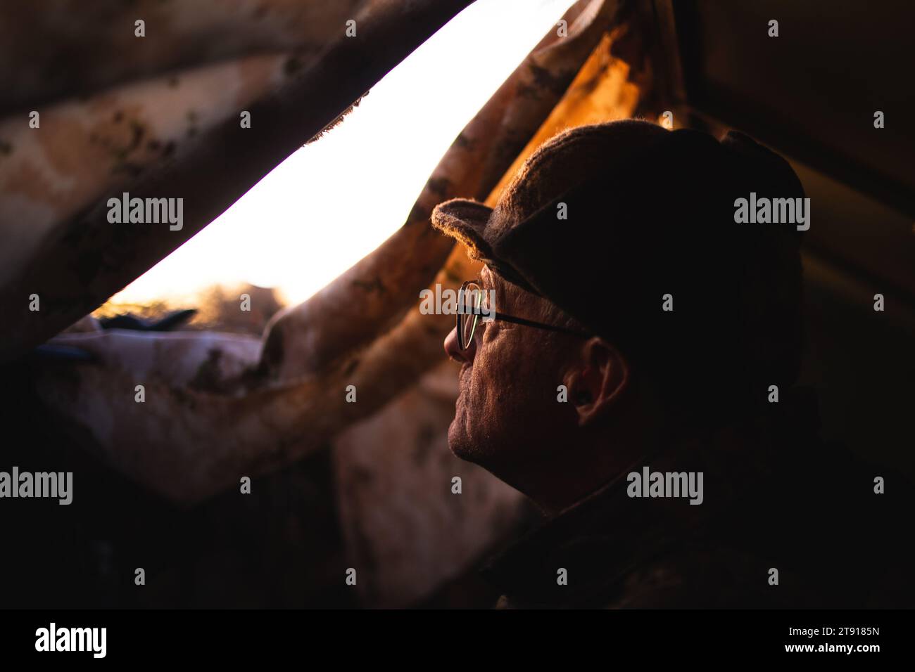 Un vecchio osserva il sole sorgere da un cieco galleggiante mentre caccia all'anatra a metà novembre mattina. I dettagli del viso e il calore sono buoni Foto Stock