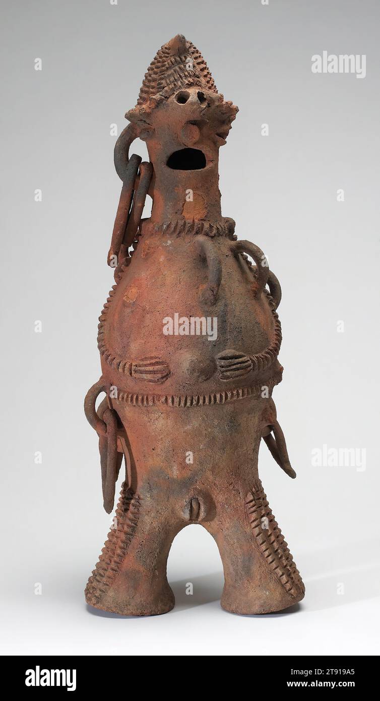 Figura femminile, inizio XX secolo, 25 7/8 x 8 9/16 x 9 9/16 pollici (65,7 x 21,8 x 24,3 cm), Terracotta, Nigeria, XX secolo, nel nord-est della Nigeria un mosaico di gruppi etnici produce arte ceramica, e non è sempre possibile attribuire una particolare terracotta a un popolo specifico. I molti anse e gli elementi pendenti di questo esempio sono più comuni sulle ceramiche prodotte dai Longuda. Questo tipo di ceramica era usato ritualmente, nelle cerimonie di divinazione e guarigione. I vasi figurativi più vecchi del Longuda normalmente si trovano su un piede singolo circolare, quindi questa figura a due zampe è probabilmente più recente Foto Stock