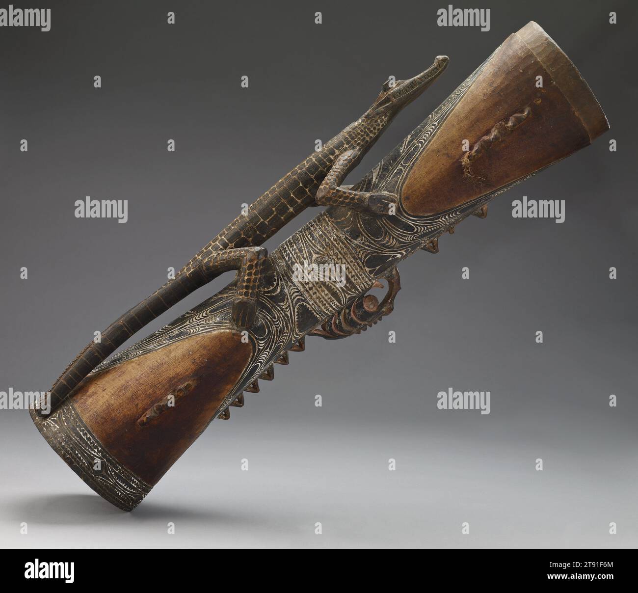 Tamburo a mano (kundu), 20° secolo, 8 1/2 x 26 3/4 x 1/2" (21,59 x 67,95 x 16,51 cm), legno, corda, pigmento a, Papua nuova Guinea, nel XX secolo, i tamburi a mano accompagnano le canzoni dei clan eseguite in importanti eventi della comunità. Il suono della batteria rappresenta lo spirito e le voci degli antenati. Gli Iatmul credono di essere discendenti da un coccodrillo gigante; questo importante animale appare molte volte su questo strumento. Il design a estremità aperta scolpito intorno a entrambe le metà del tamburo rappresenta le ganasce spalancate di due coccodrilli, simboliche di cielo e terra. Questi reami opposti sono collegati dalla maniglia del tamburo Foto Stock