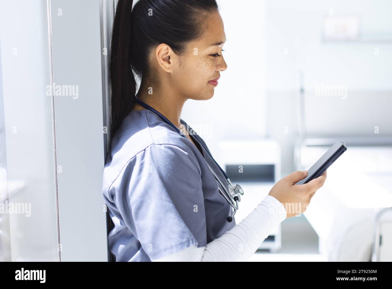 Medico femminile birazziale che indossa scrub usando smartphon in ospedale. Medicina, sanità, comunicazione, lavoro e ospedale, inalterati. Foto Stock