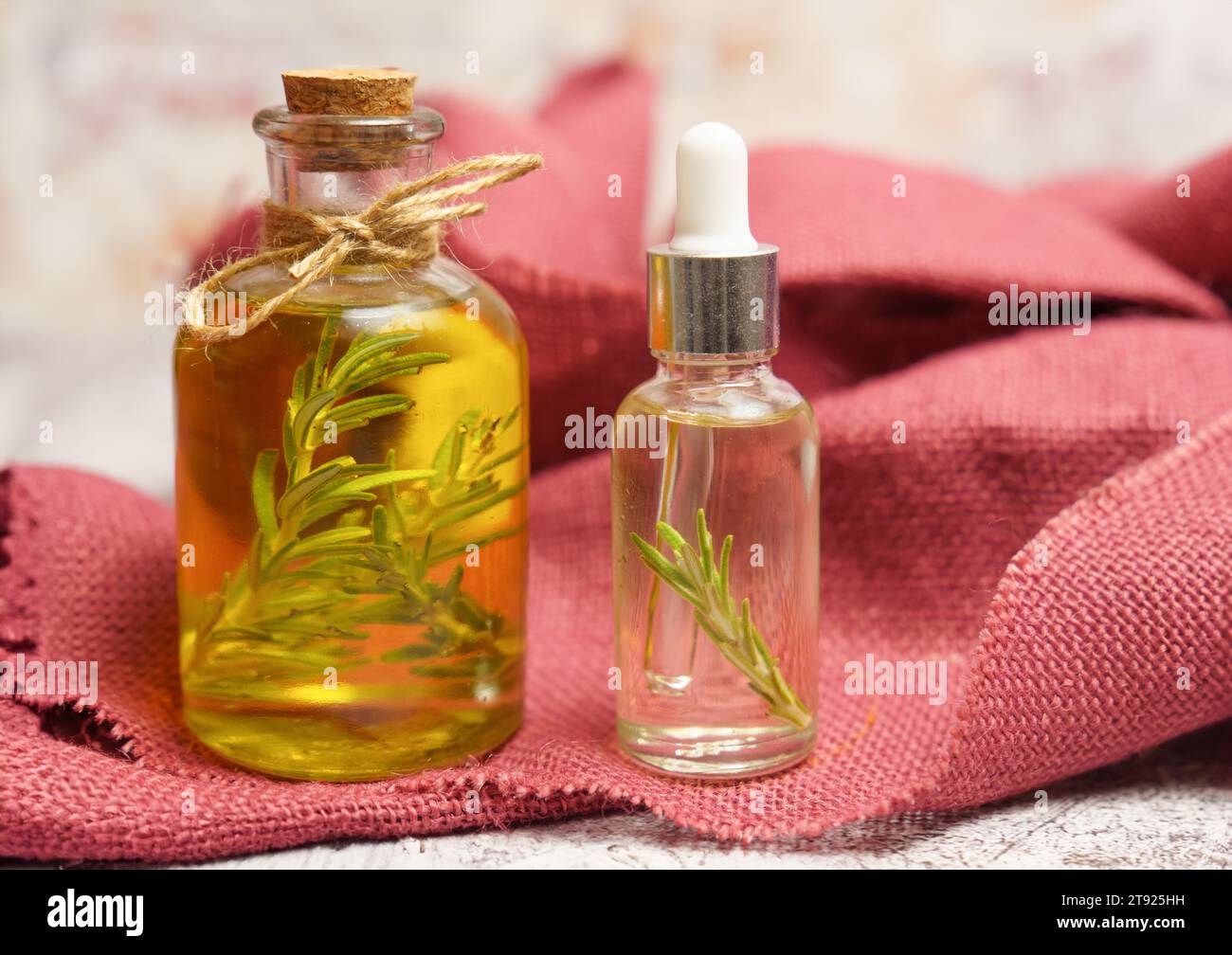 Bottiglia e contagocce con olio di rosmarino con ramoscelli freschi all'interno su un panno rosso Foto Stock