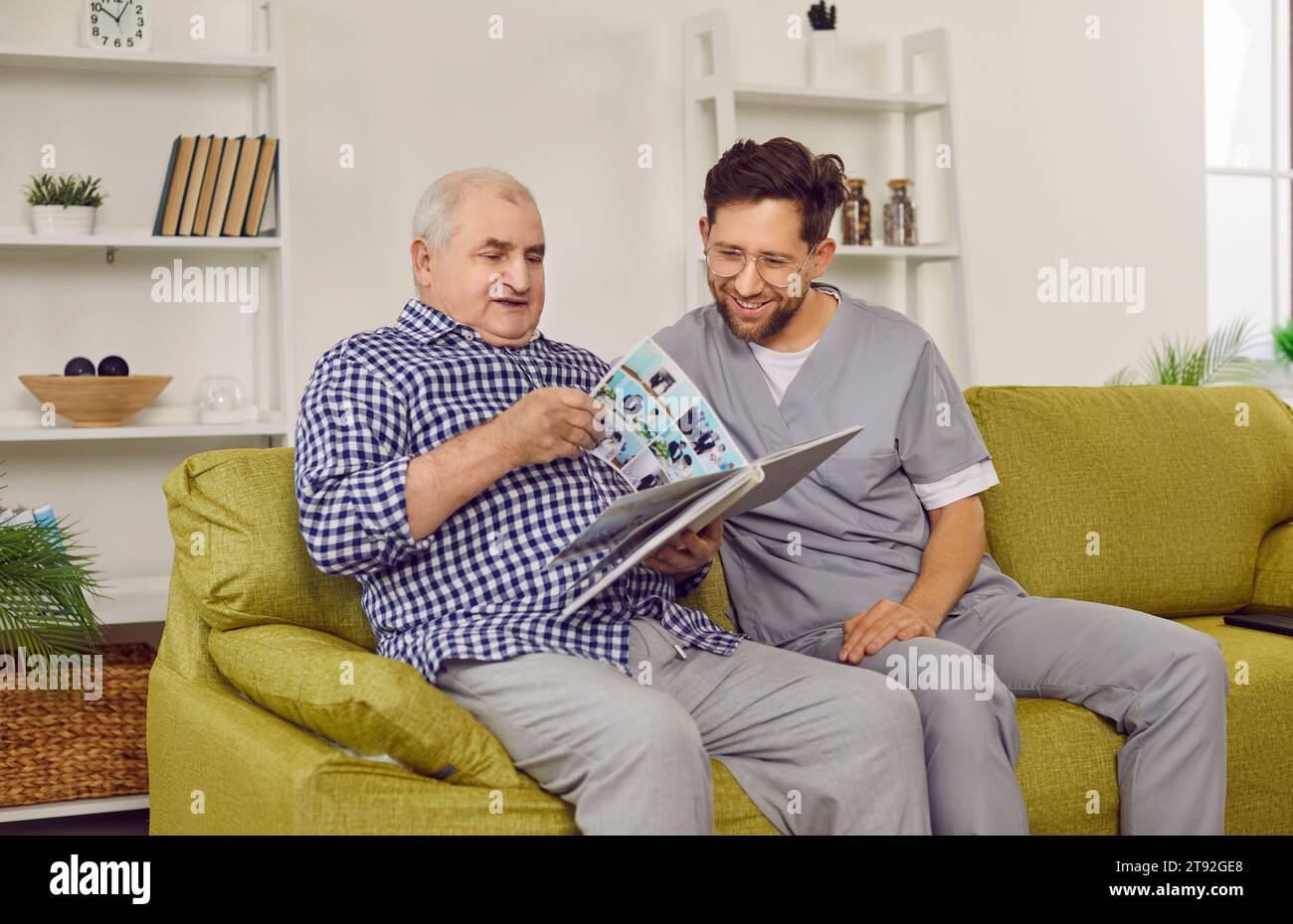 Uomo anziano e giovane uomo che guarda un album fotografico di famiglia in salotto Foto Stock
