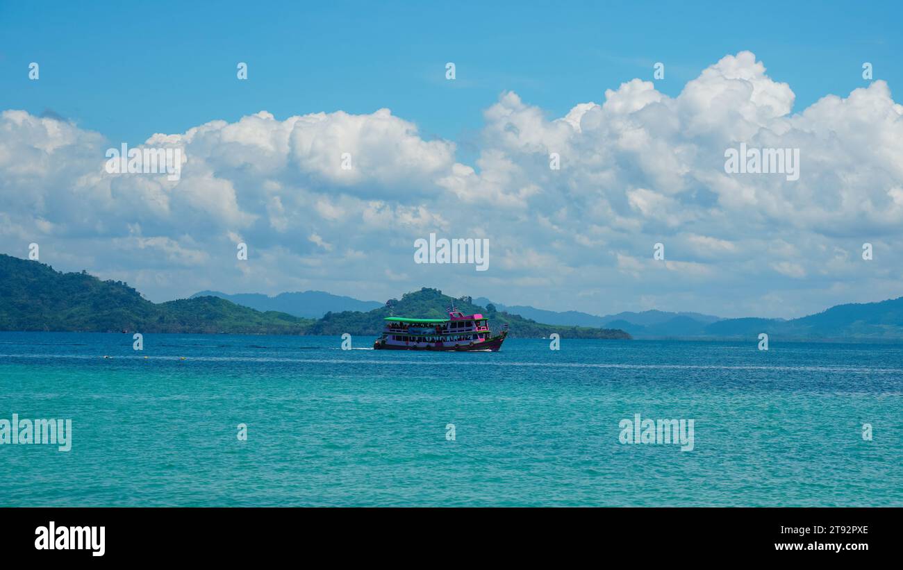 Paesaggio tropicale. Naviga nelle acque turchesi dell'oceano contro il cielo blu con le nuvole bianche e l'isola tropicale. Paesaggio naturale per le vacanze estive, panor Foto Stock