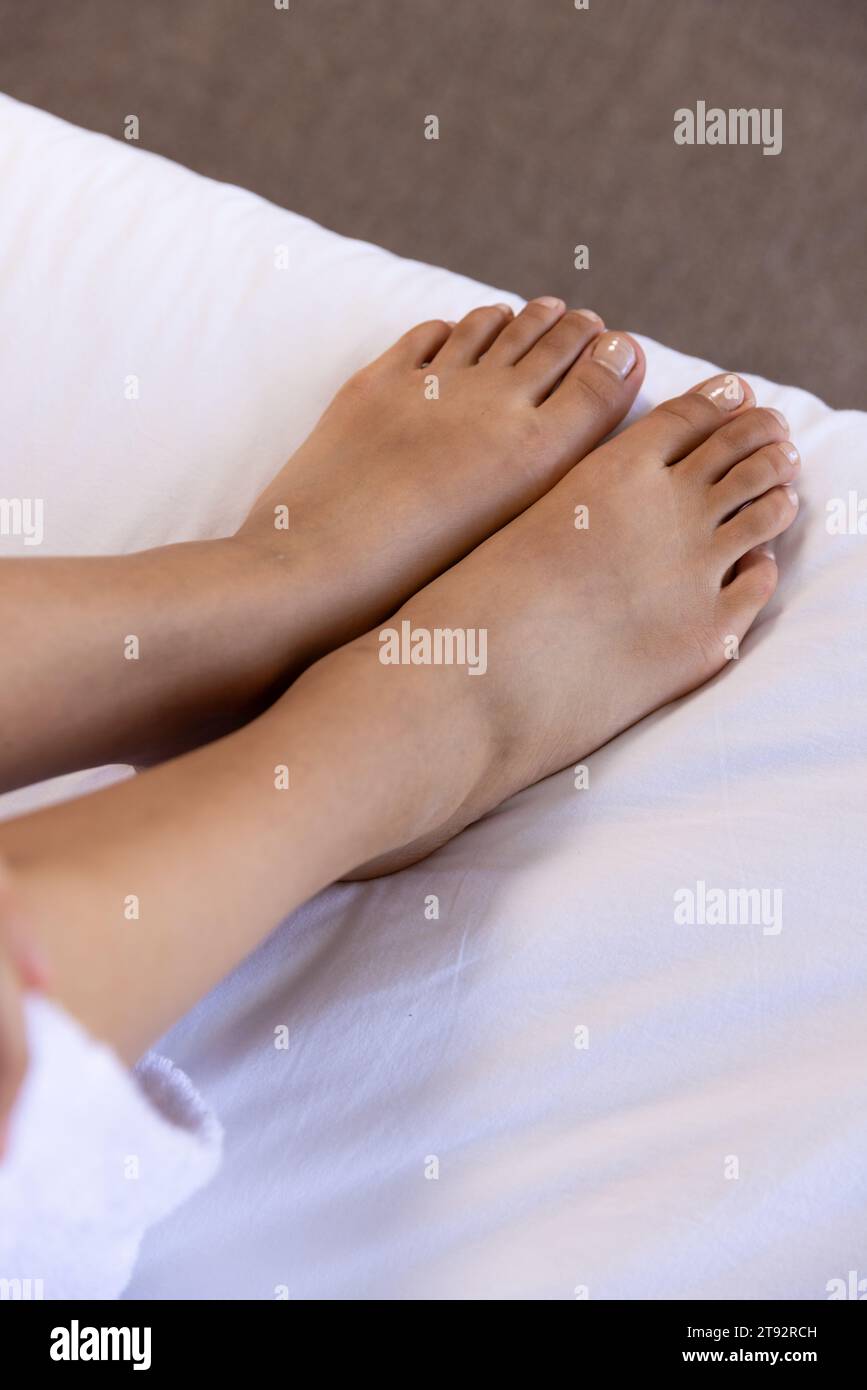 Gambe di donna birazziale sdraiate sul letto a casa soleggiata. Stile di vita, tempo libero e vita domestica, inalterati. Foto Stock