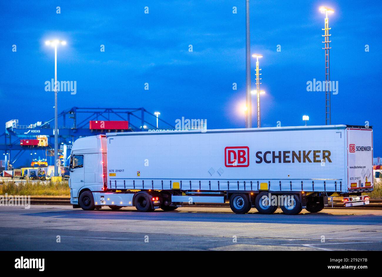 PRODUZIONE - 21 novembre 2023, Meclemburgo-Pomerania Occidentale, Rostock: Un camion con rimorchi della società di logistica DB Schenker si trova sul sito del centro logistico nel porto marittimo la mattina. La filiale logistica di Deutsche Bahn gestisce diversi centri logistici nel Meclemburgo-Pomerania. Foto: Jens Büttner/dpa Foto Stock