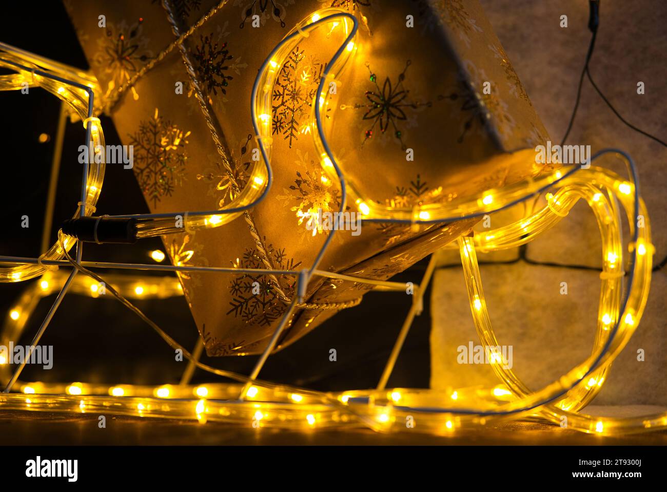 Tuffati nello spirito natalizio con un primo piano di un regalo di Natale avvolto in carta dorata adornata da scintillanti fiocchi di neve. L'angolo inferiore del gif Foto Stock