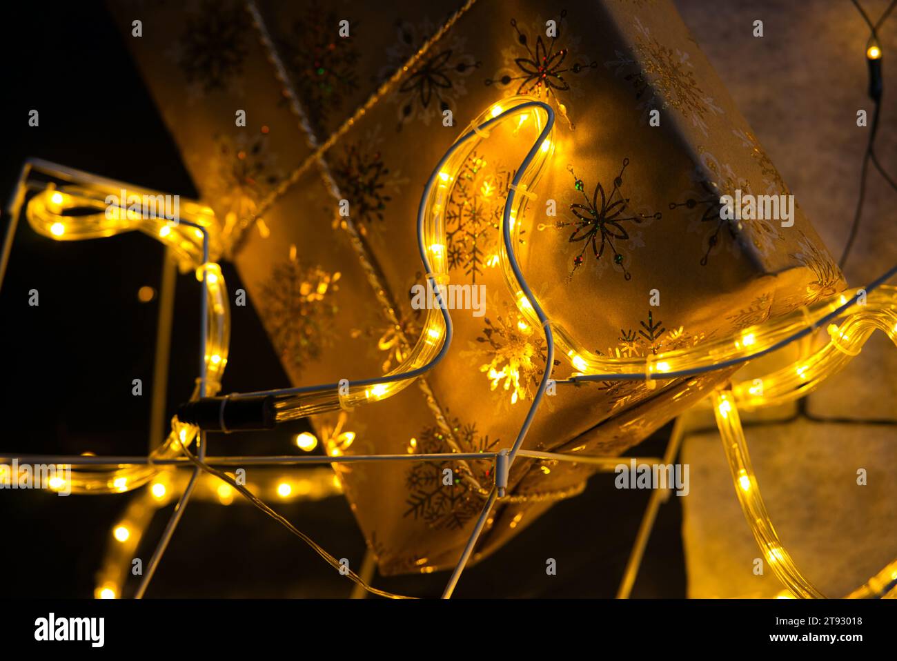 Tuffati nello spirito natalizio con un primo piano di un regalo di Natale avvolto in carta dorata adornata da scintillanti fiocchi di neve. L'angolo inferiore del gif Foto Stock