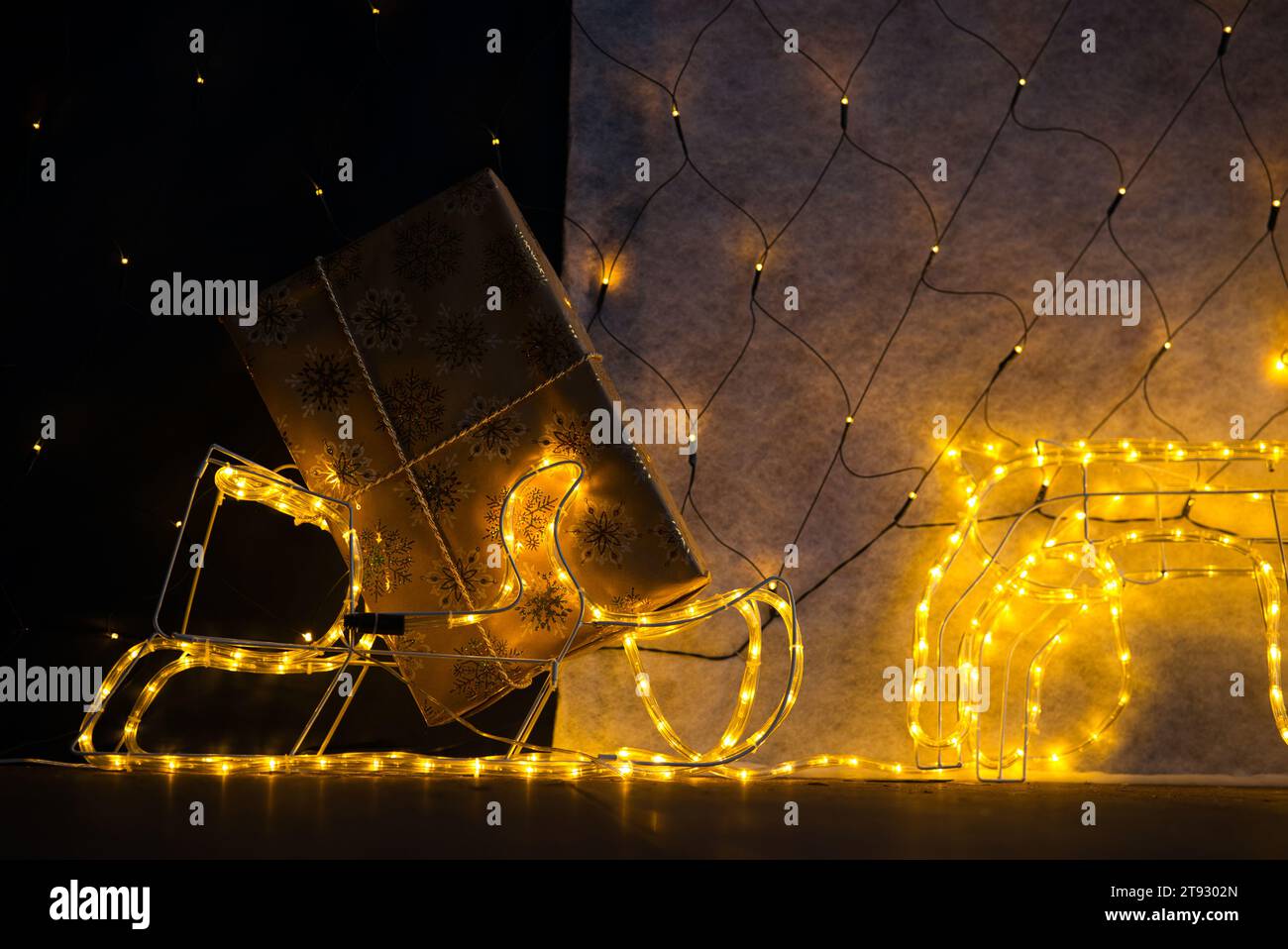 Tuffati nello spirito natalizio con un primo piano di un regalo di Natale avvolto in carta dorata adornata da scintillanti fiocchi di neve. L'angolo inferiore del gif Foto Stock