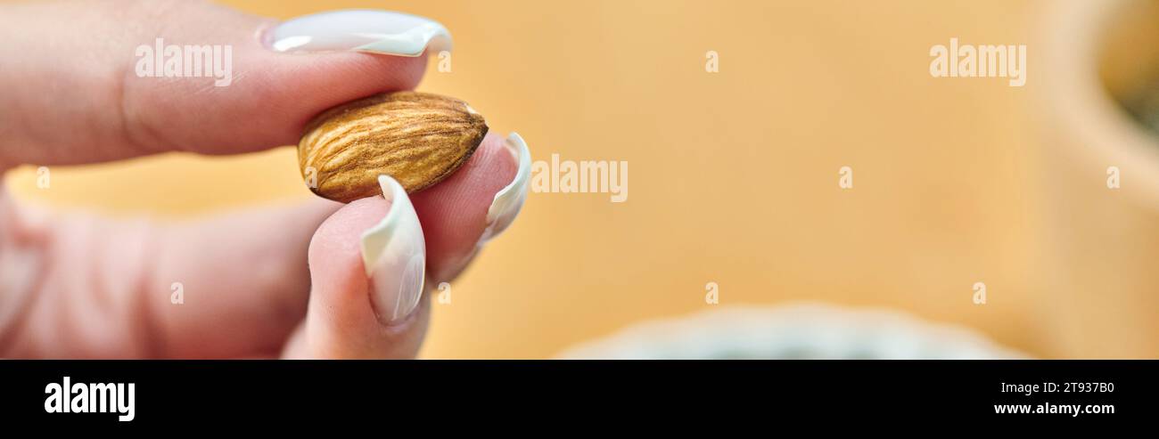 vista ravvicinata di una donna vegetariana dal taglio corto con deliziose mandorle, dieta sana a base di piante, striscione Foto Stock