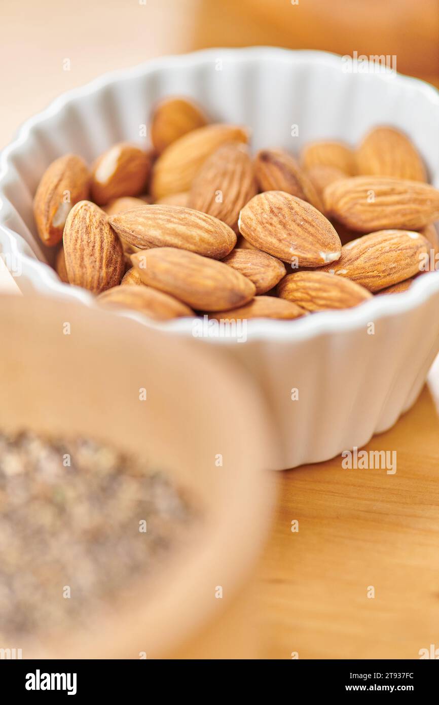 vista ravvicinata delle deliziose mandorle in un recipiente in ceramica bianca su diete a base di piante in primo piano sfocate Foto Stock