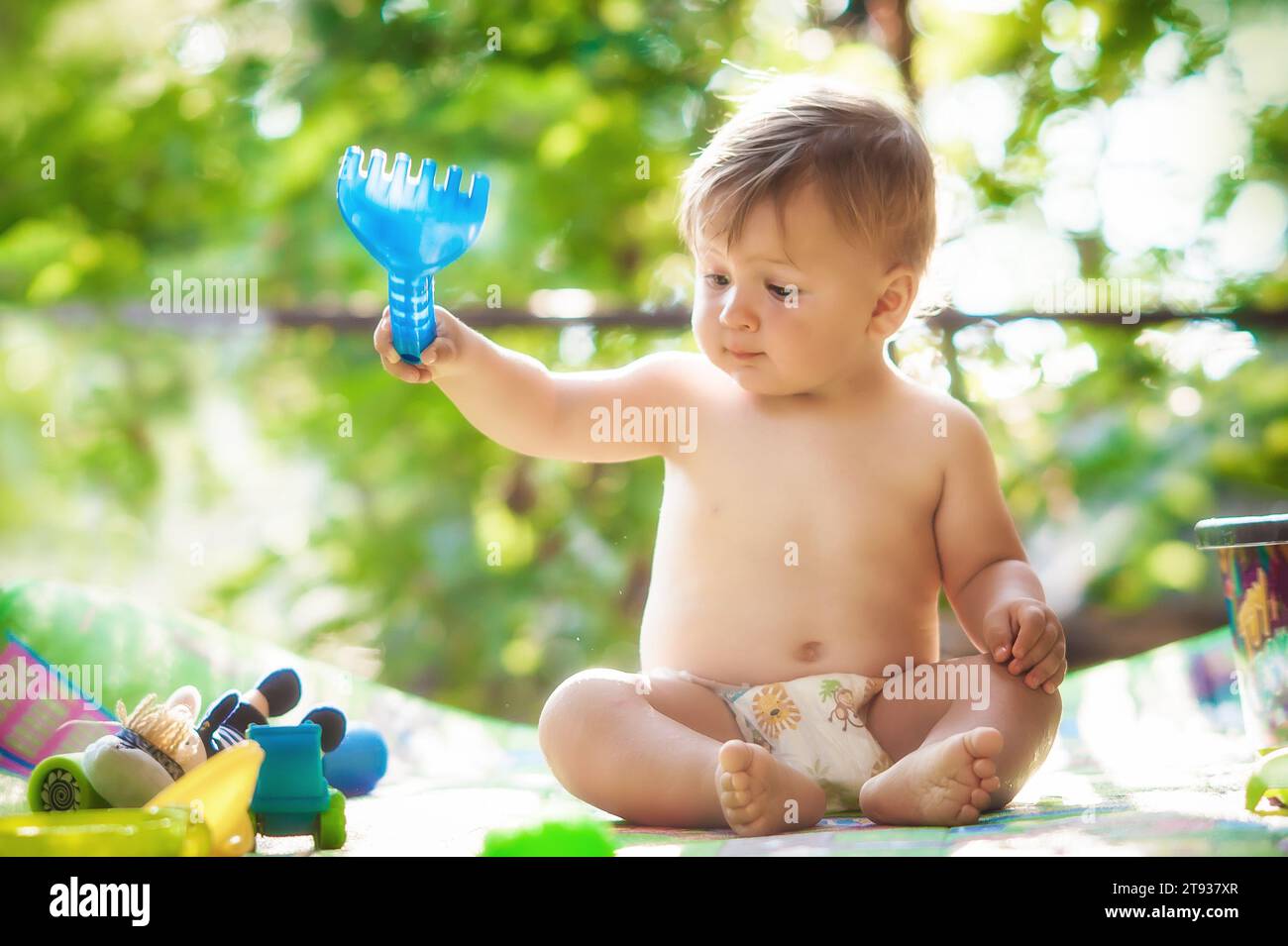 Bambino seduto in giardino e che gioca con i giochi d'acqua. Calda giornata estiva nella natura Foto Stock