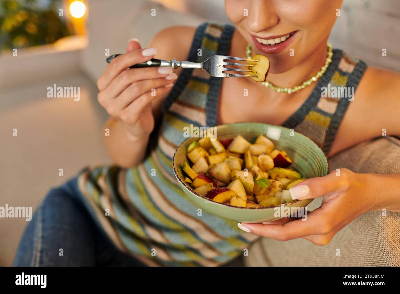 vista a ritaglio di una donna vegetariana che mangia una deliziosa macedonia di frutta per cena sul divano nel soggiorno Foto Stock