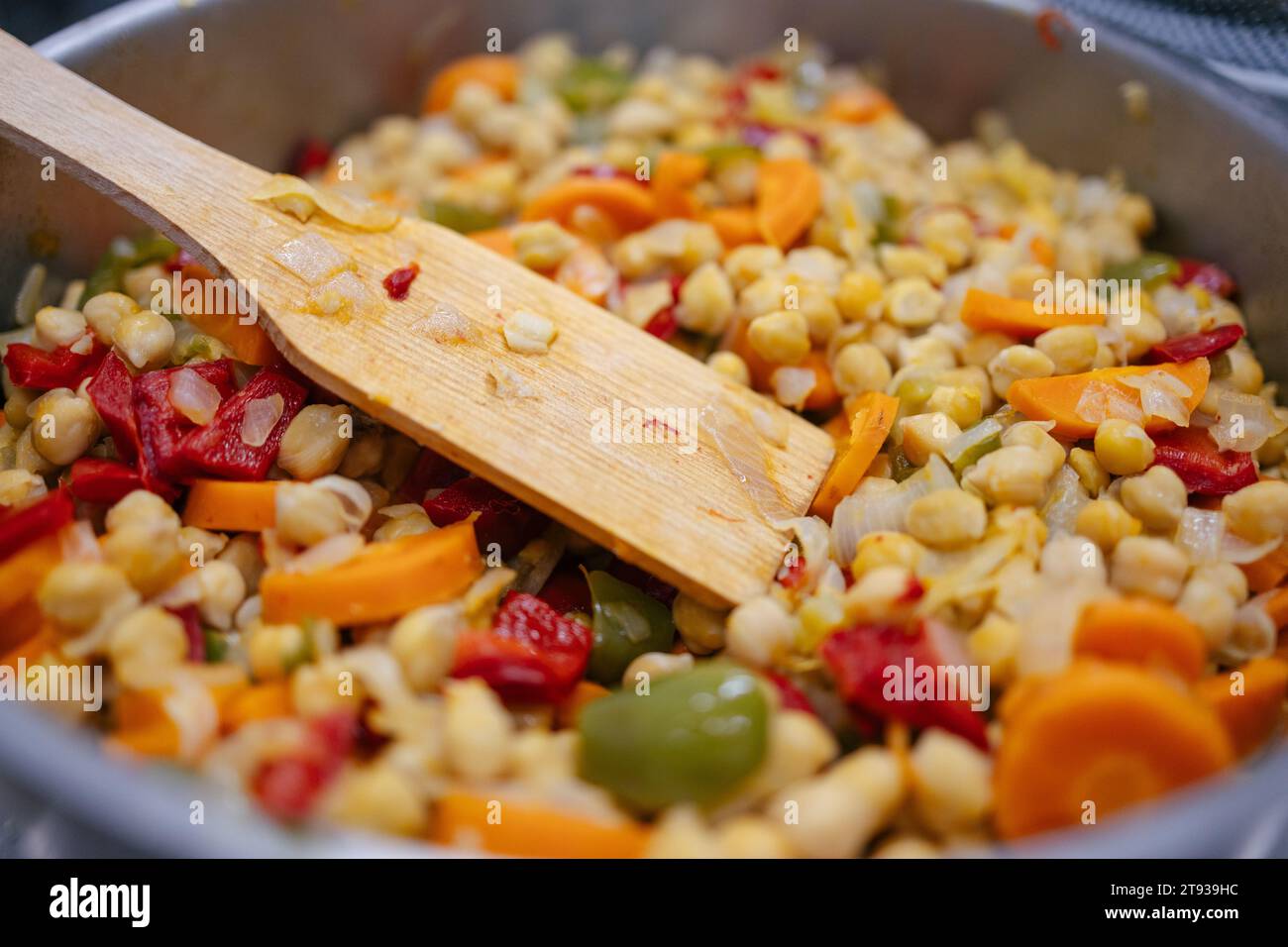 Primo piano di una pentola con verdure e ceci e una spatola per mescolare mentre cucinano Foto Stock