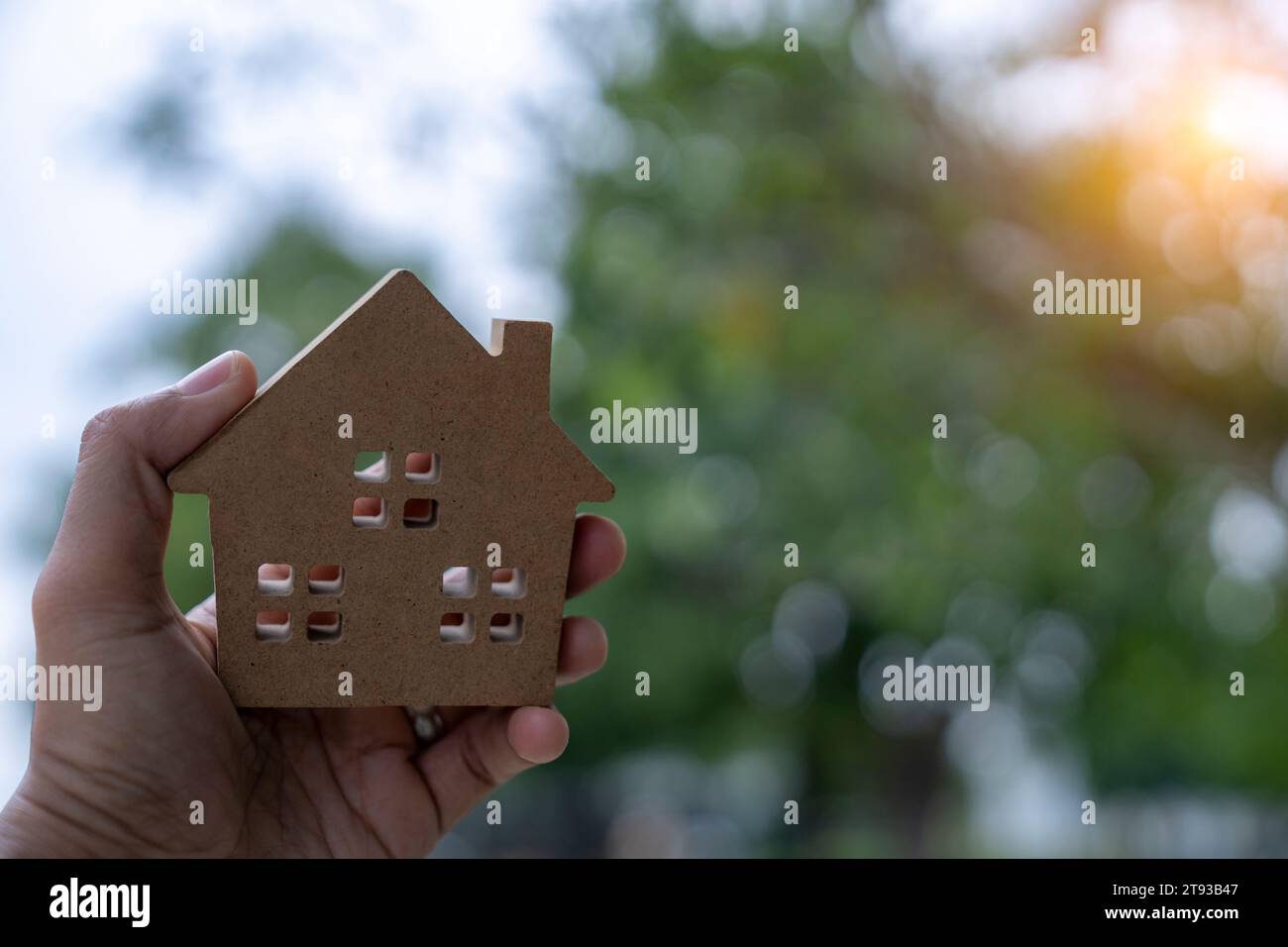 Casa modello in miniatura in mano con sfondo luminoso bokeh Foto Stock