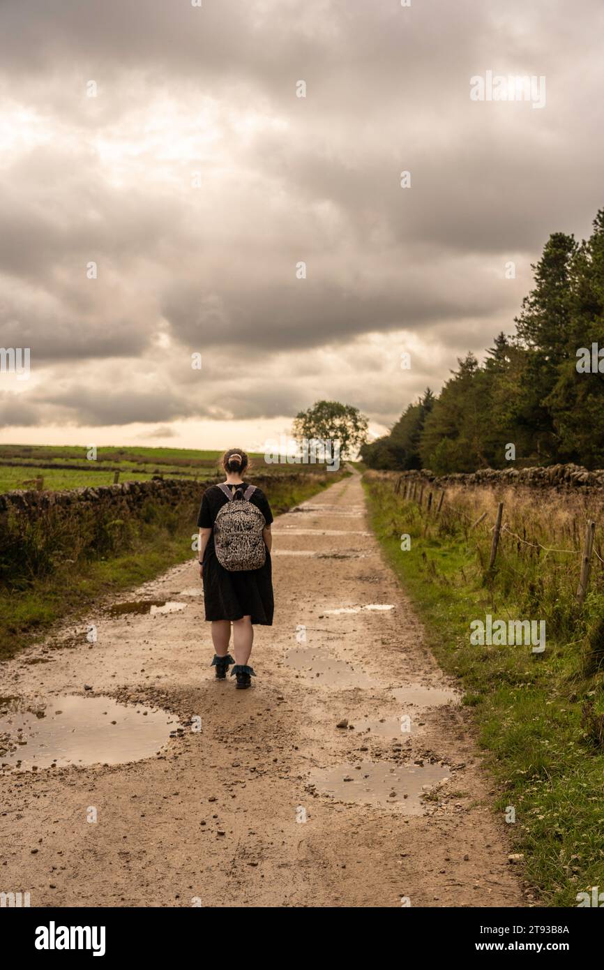 Ragazza vestita che si allontana dalla macchina fotografica lungo una pista umida e fangosa a Osmotherly, North Yorkshire, Inghilterra, Regno Unito Foto Stock