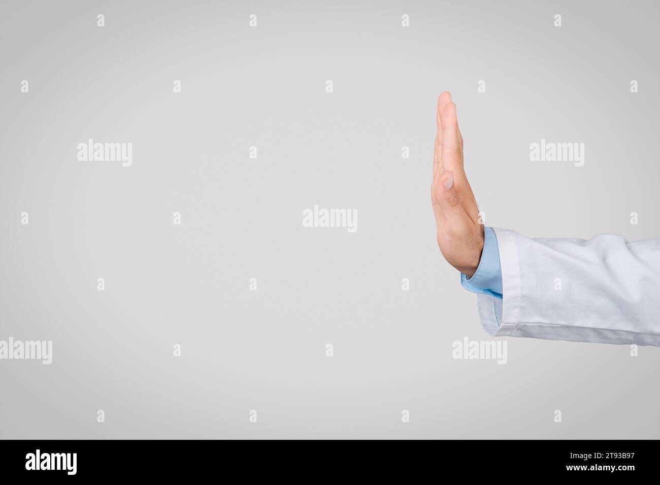 Medico maschio in camice bianco con gesto stop, vista laterale, sfondo grigio, spazio libero Foto Stock