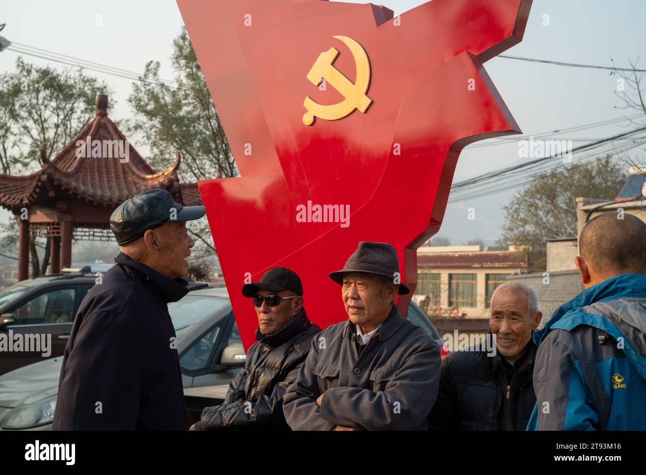 Gli anziani siedono di fronte a una scultura di una bandiera rossa con il logo del Partito Comunista a Pechino, in Cina. 21 novembre 2023 Foto Stock