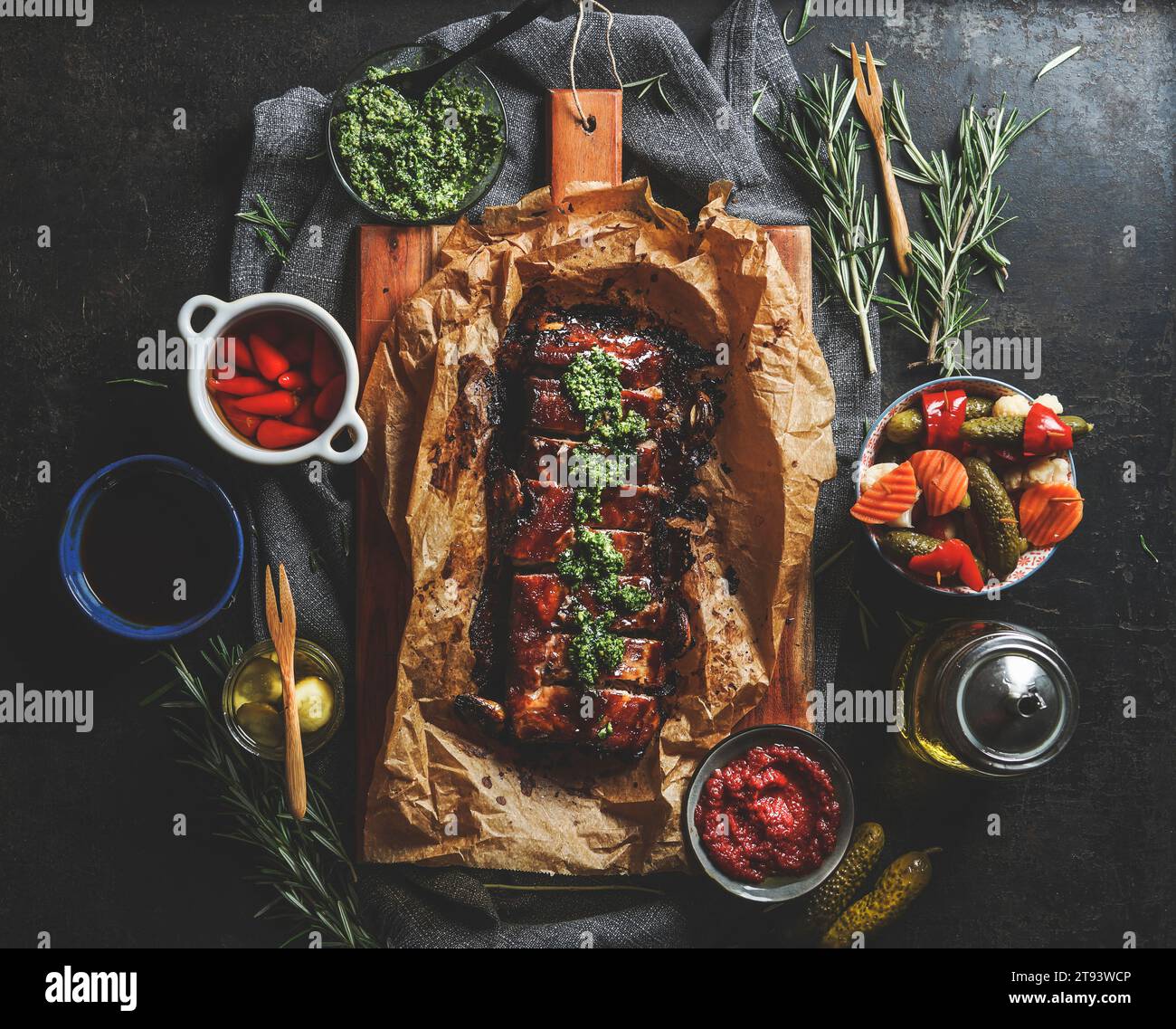 Costolette grigliate arrosto con pesto fatto in casa, verdure sottaceto, salse e rosmarino su tavolo da cucina in cemento scuro. Saporito di carne condita per cena. Superiore Foto Stock