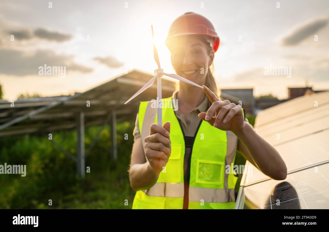Ingegnere sorridente in possesso di un modello di turbina eolica in un impianto solare. Immagine del concetto ecologico di energia alternativa. Foto Stock