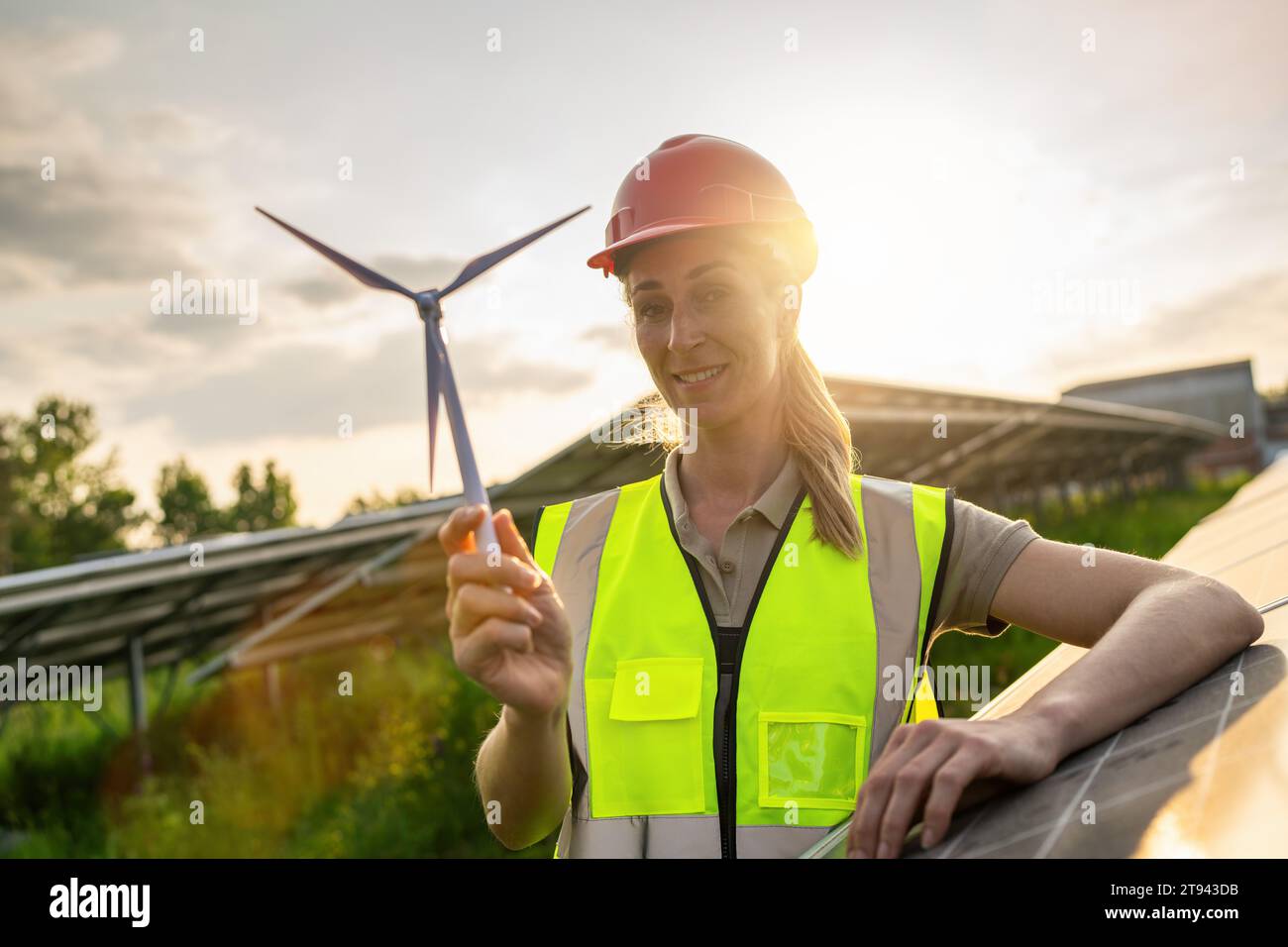 Ingegnere donna con modello di turbina eolica presso il sistema di pannelli fotovoltaici dell'azienda di energia solare al tramonto. Concetto ecologico di energia alternativa. Foto Stock
