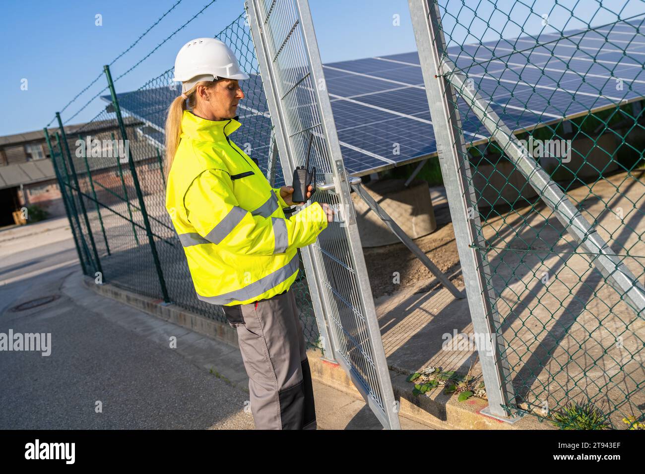 Tecnico in giacca ad alta visibilità su un cancello con walkie-talkie presso l'impianto solare. Immagine del concetto ecologico di energia alternativa. Foto Stock