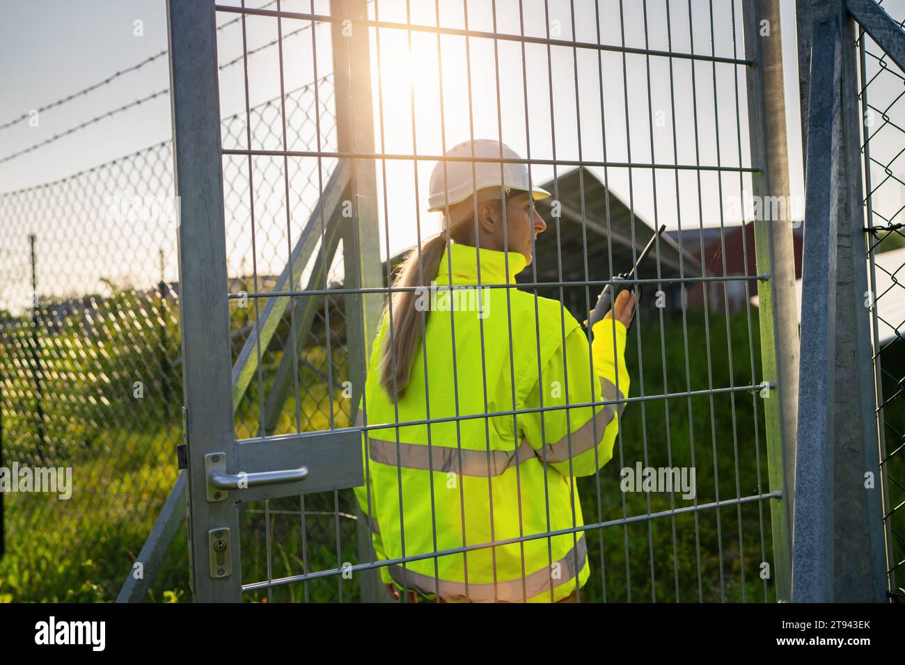 Tecnico donna con walkie-talkie che cammina verso il cancello del campo solare Foto Stock